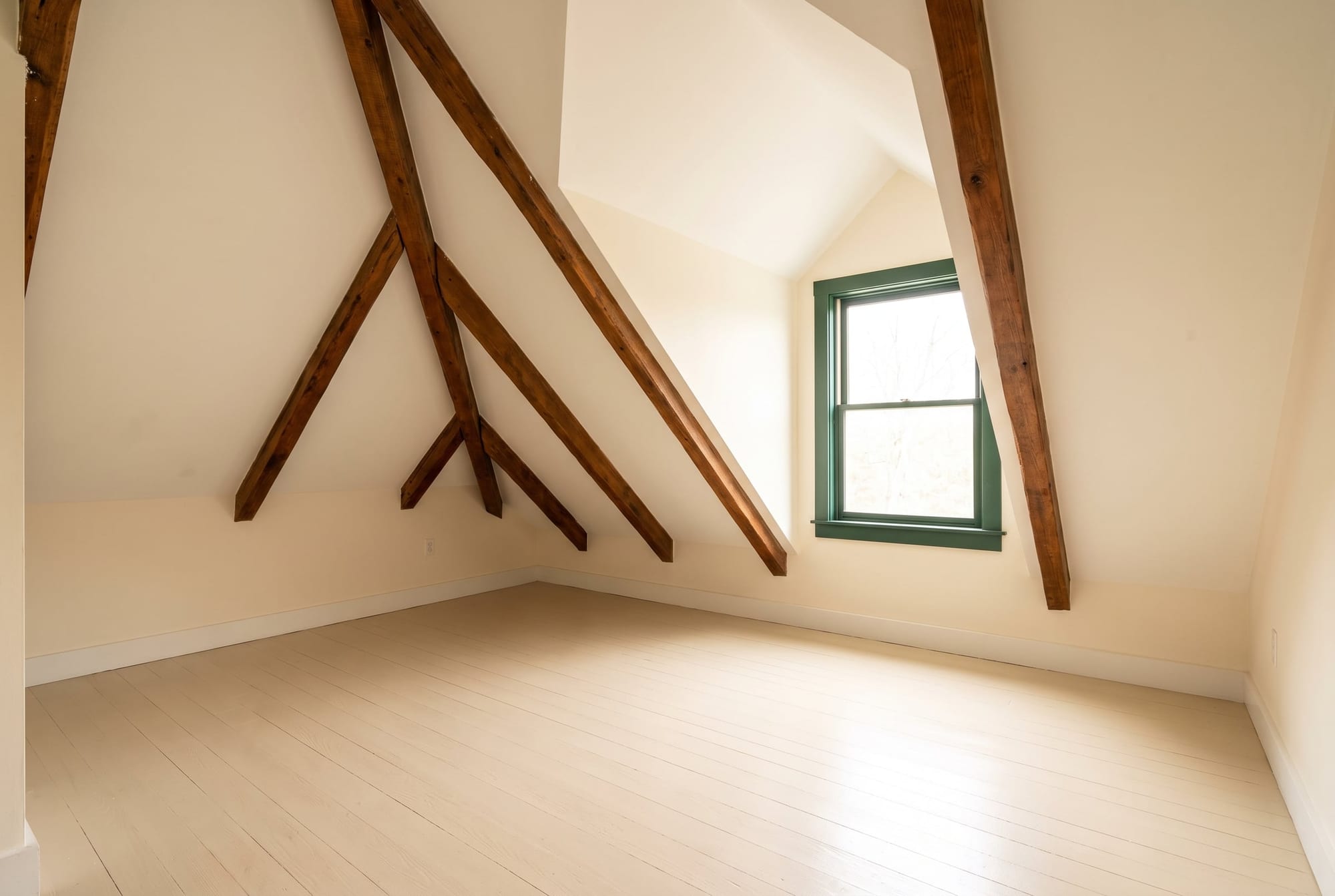 Empty attic bedroom with sloped ceilings, exposed beams and a dormer window in a house for sale