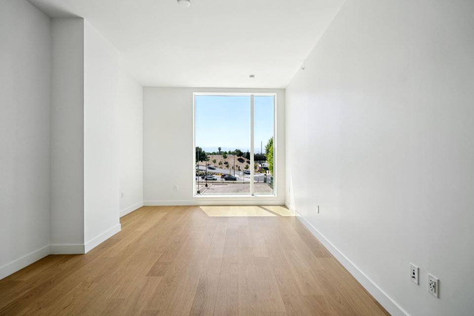 Empty bedroom before virtual staging, with a tall window at the far end